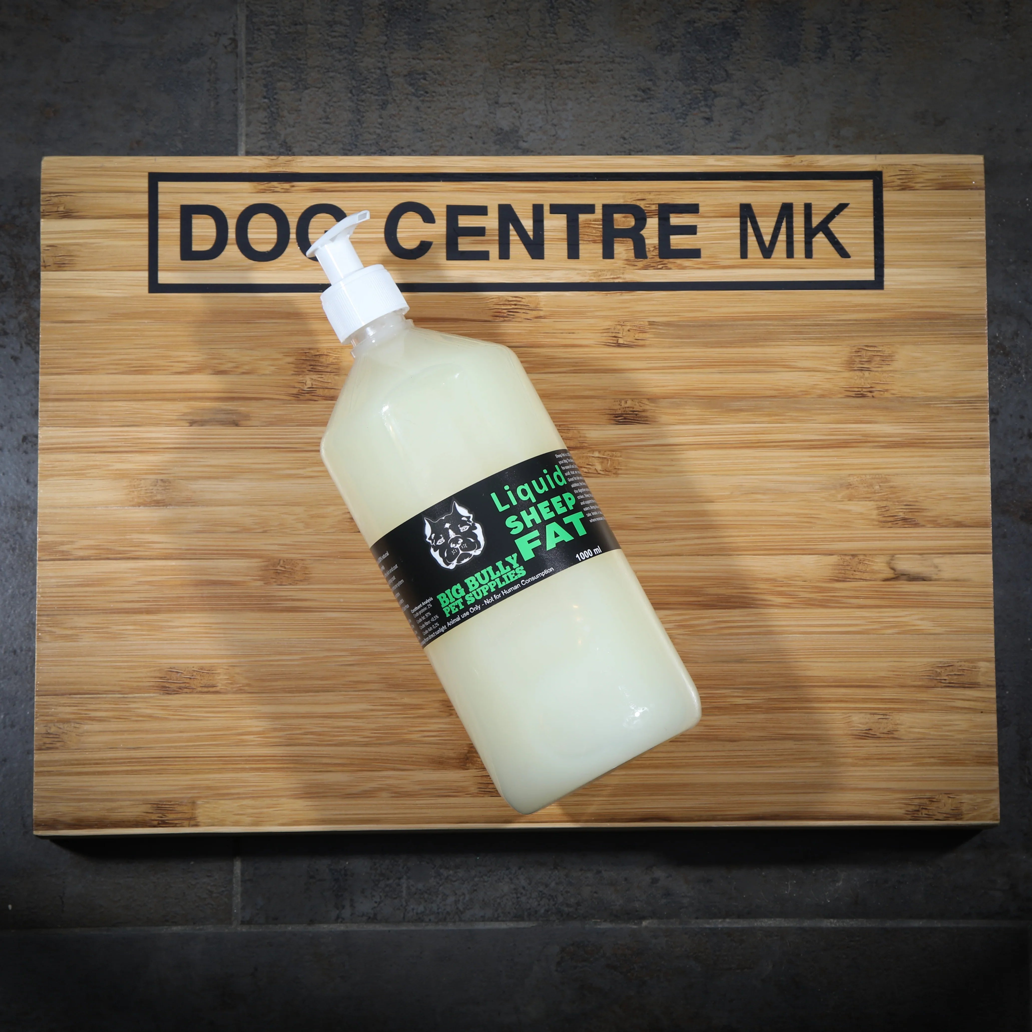 A bottle of sheep fat on a wooden board with 'DOG CENTRE MK' printed on it.