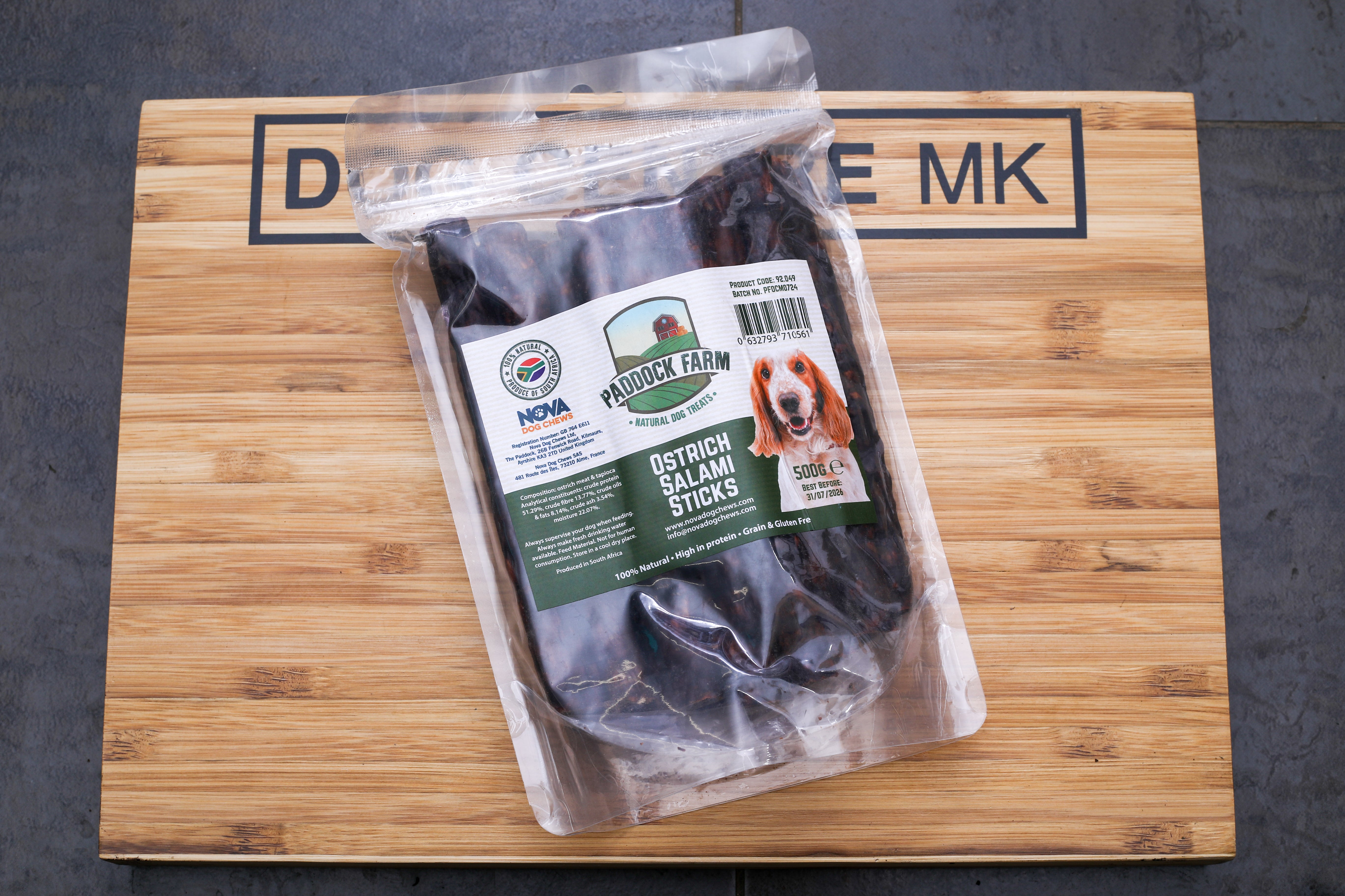 Packaged ostrich salami sticks on a wooden board with the brand 'Dog MK' visible on the packaging.