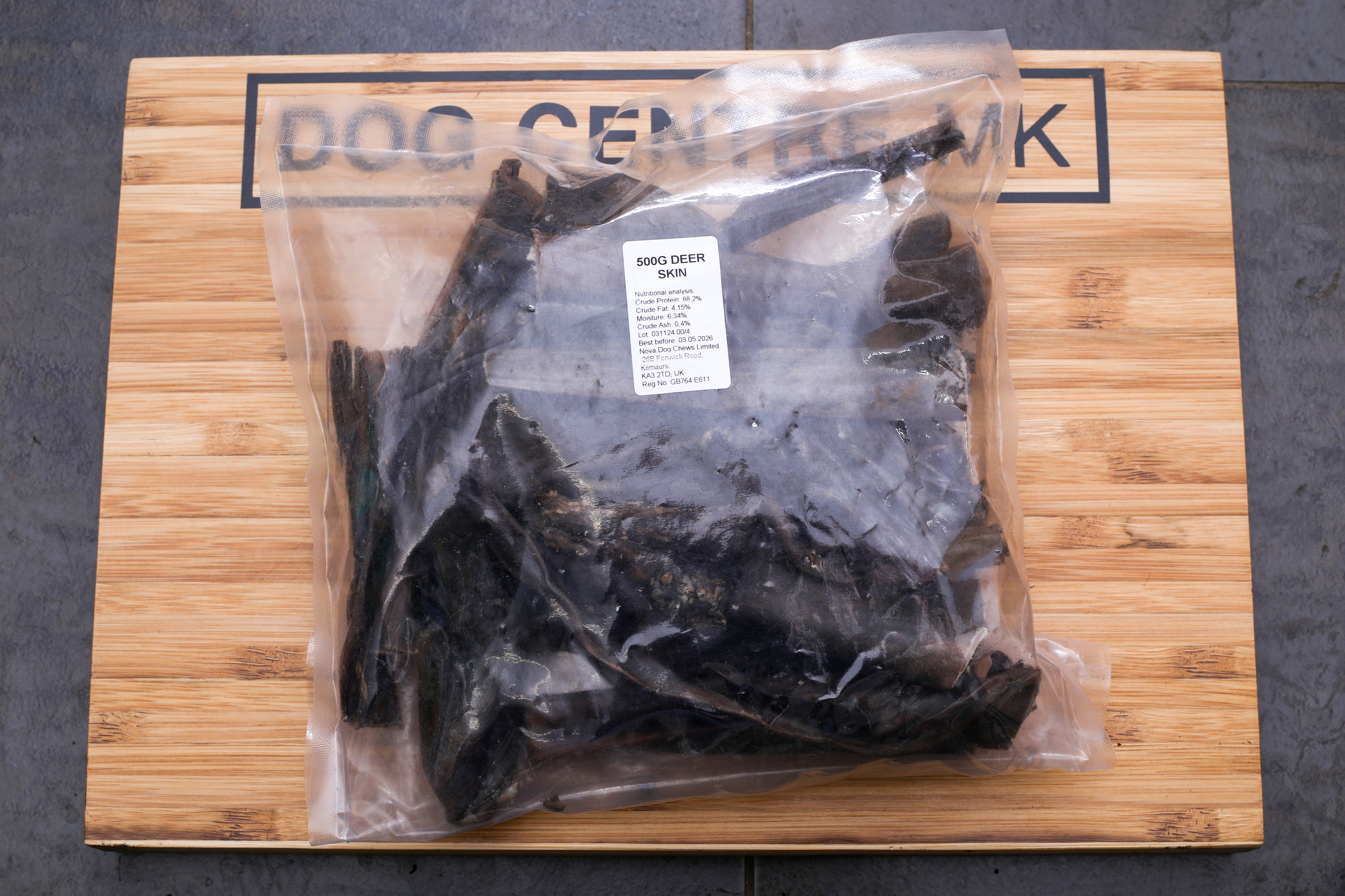 A plastic-wrapped 500g package of deer skin on a wooden surface with 'DOG CENTRE MK' printed in black on the wooden edge.