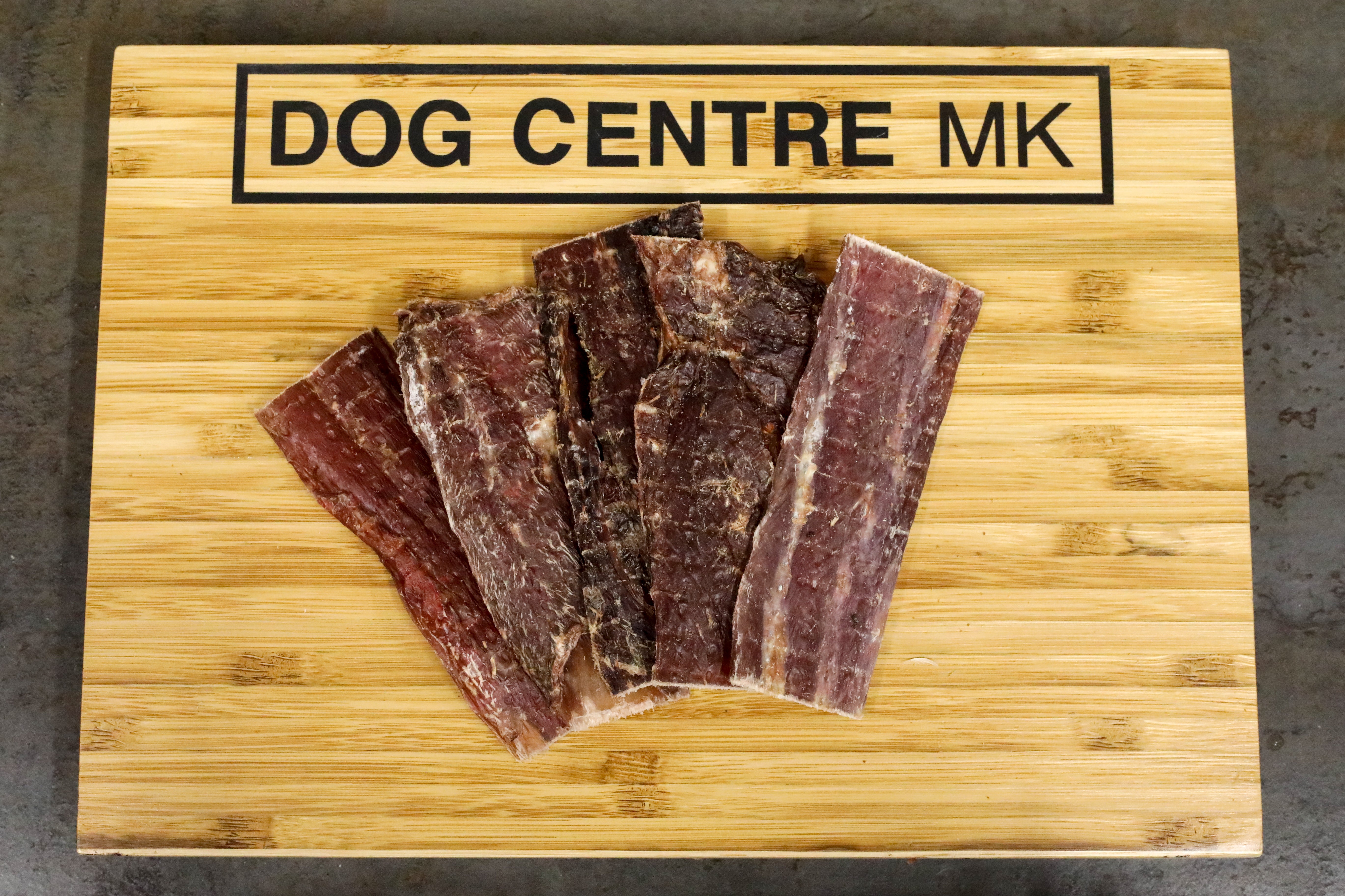 flat strips of dried meat on dog centre mk branded wooden board
