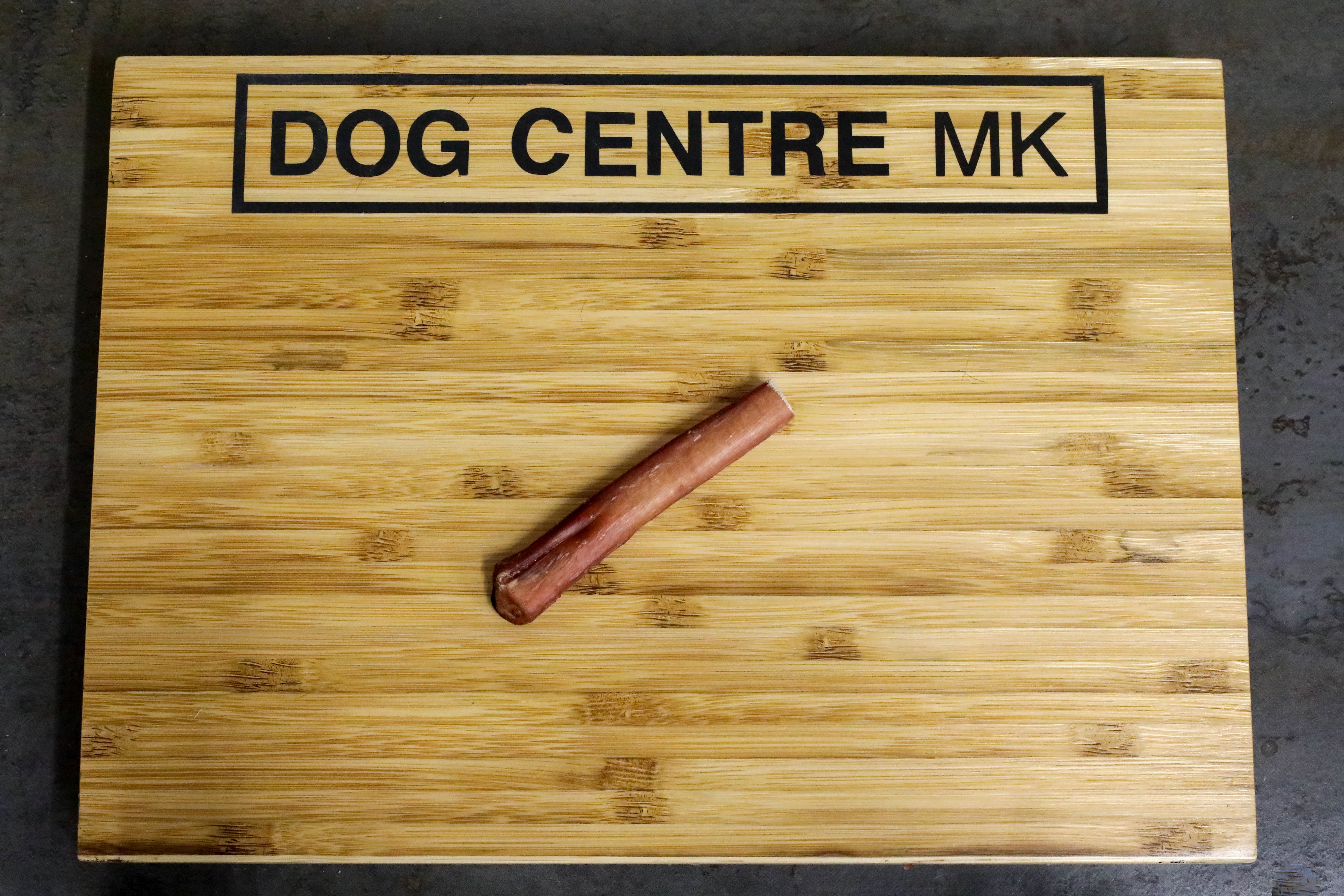 A bull pizzle with 'DOG CENTRE MK' printed on the wooden board it is laid on