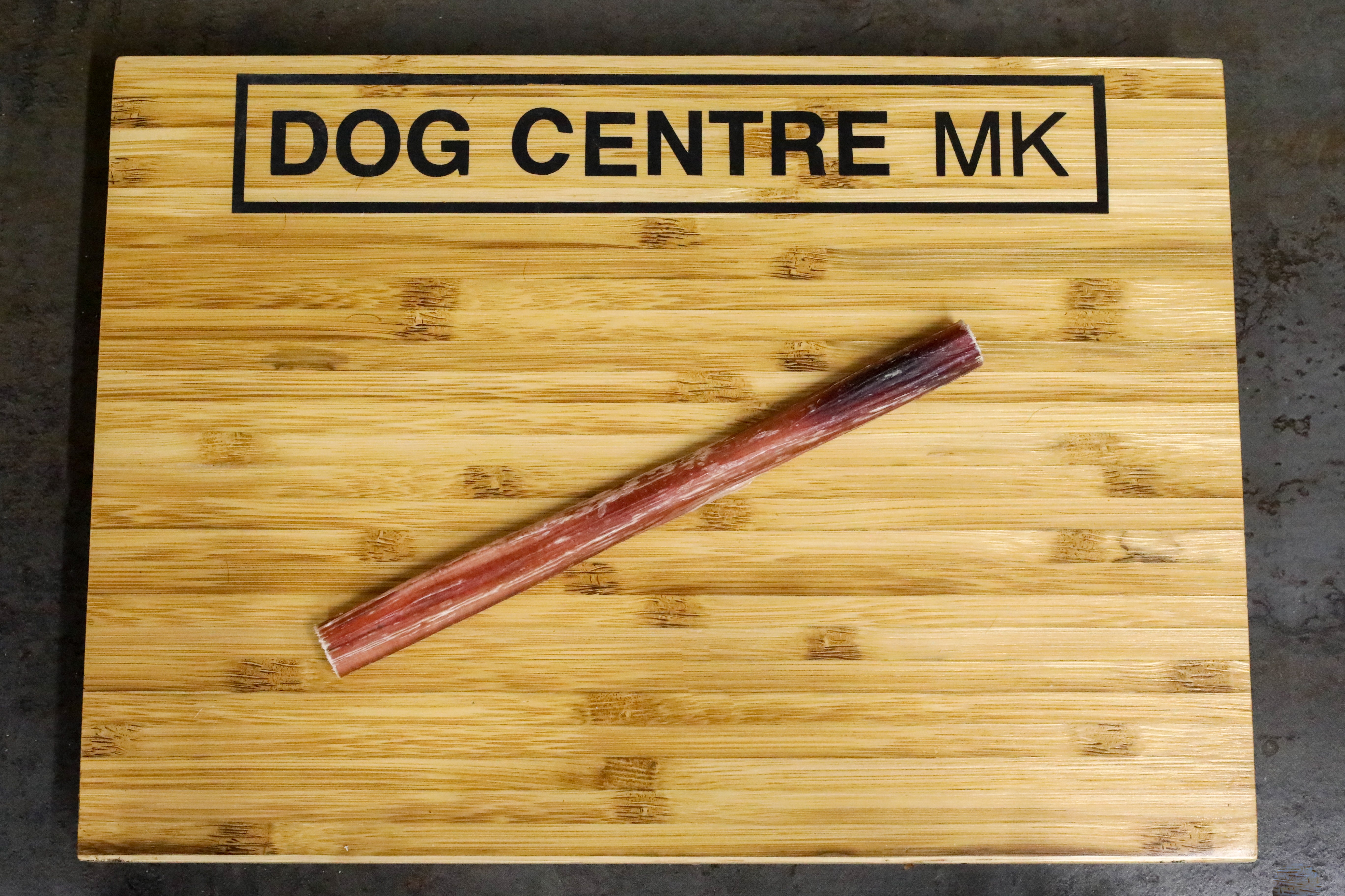 A bull pizzle with 'DOG CENTRE MK' engraved on the surface, placed on a wooden board.