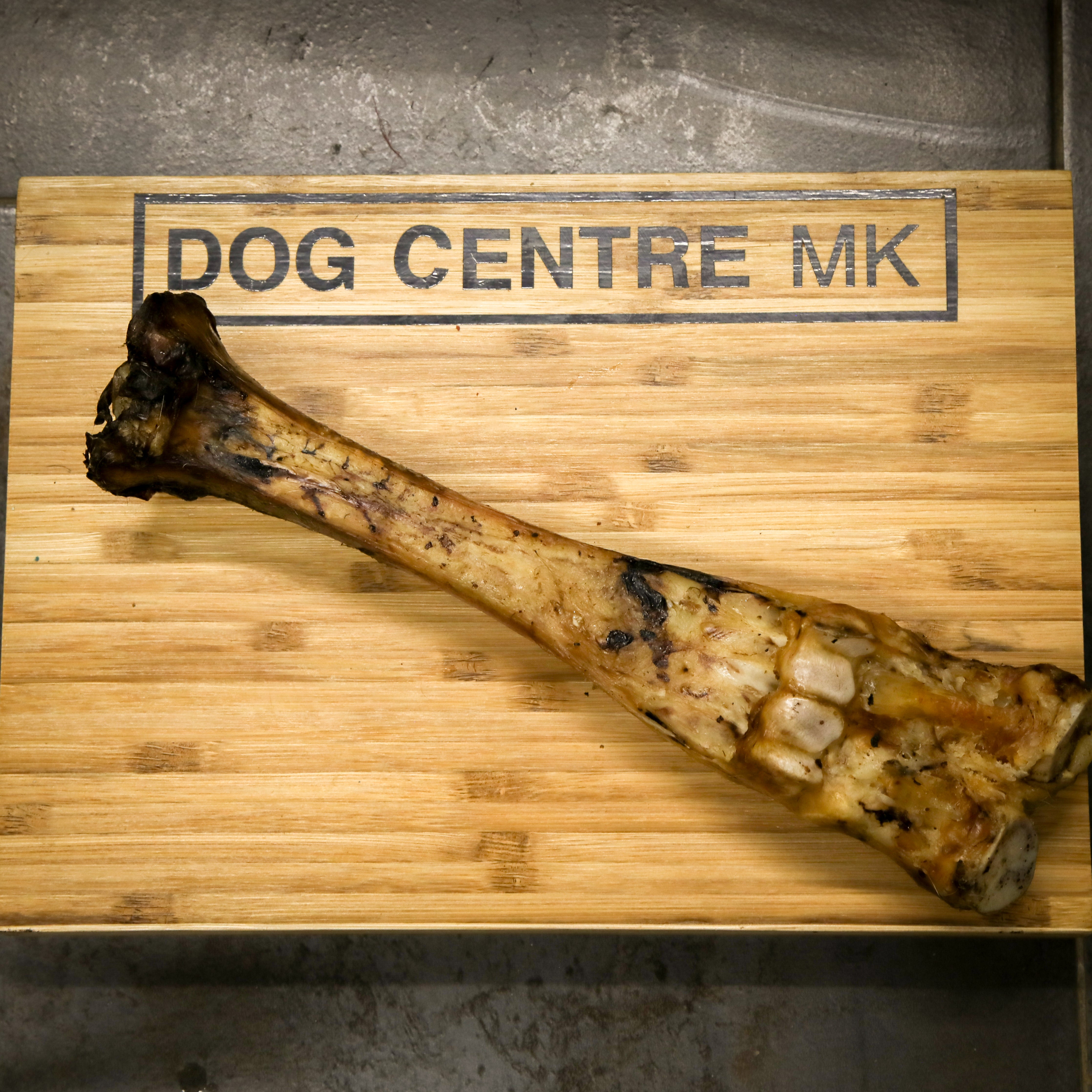 beef leg bone on a wooden board with 'DOG CENTRE MK' branding.