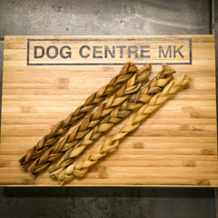 4 braided dog treats on a wooden board with 'DOG CENTRE MK' branding.