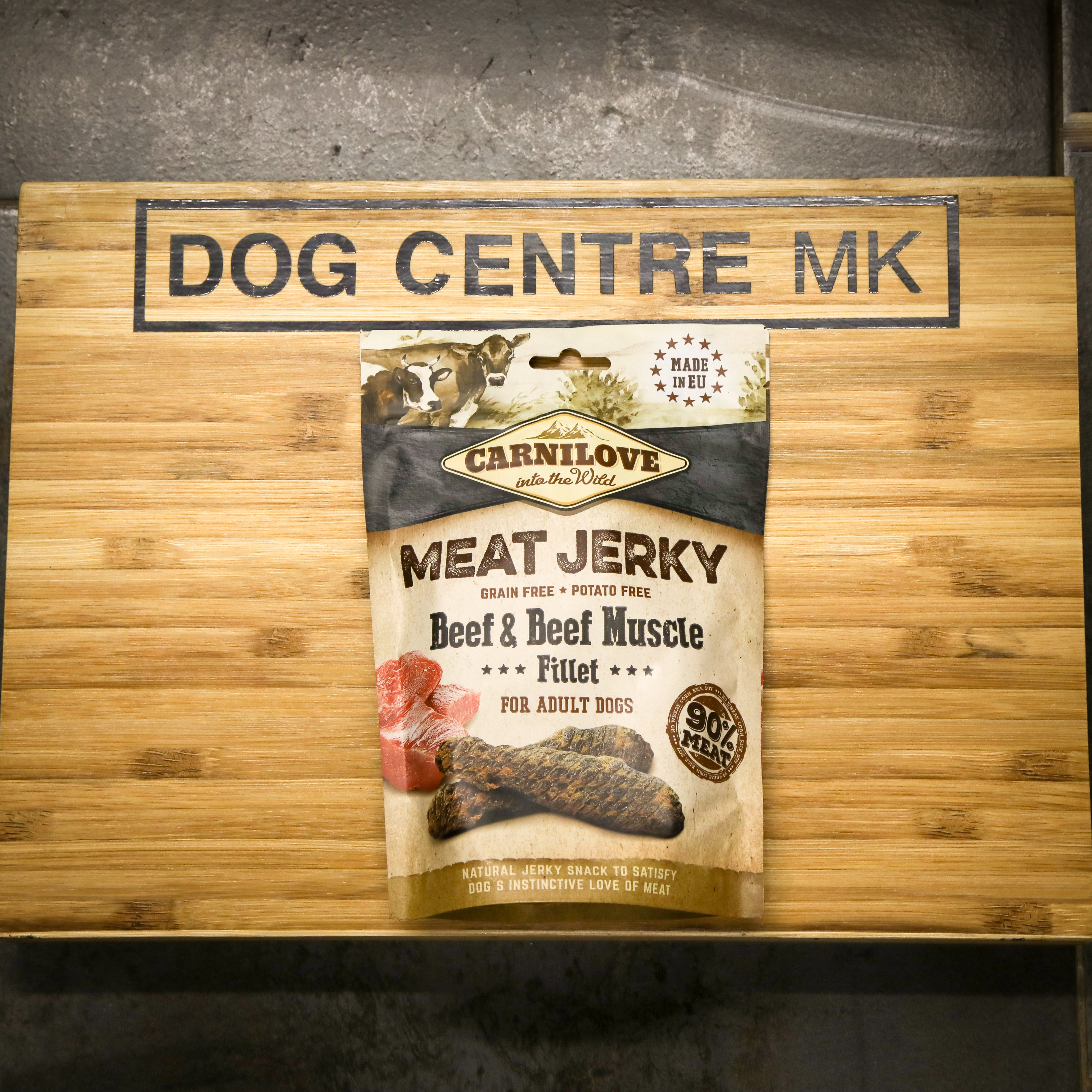 Carnilove meat jerky package on a wooden board with 'Dog Centre MK' branding.