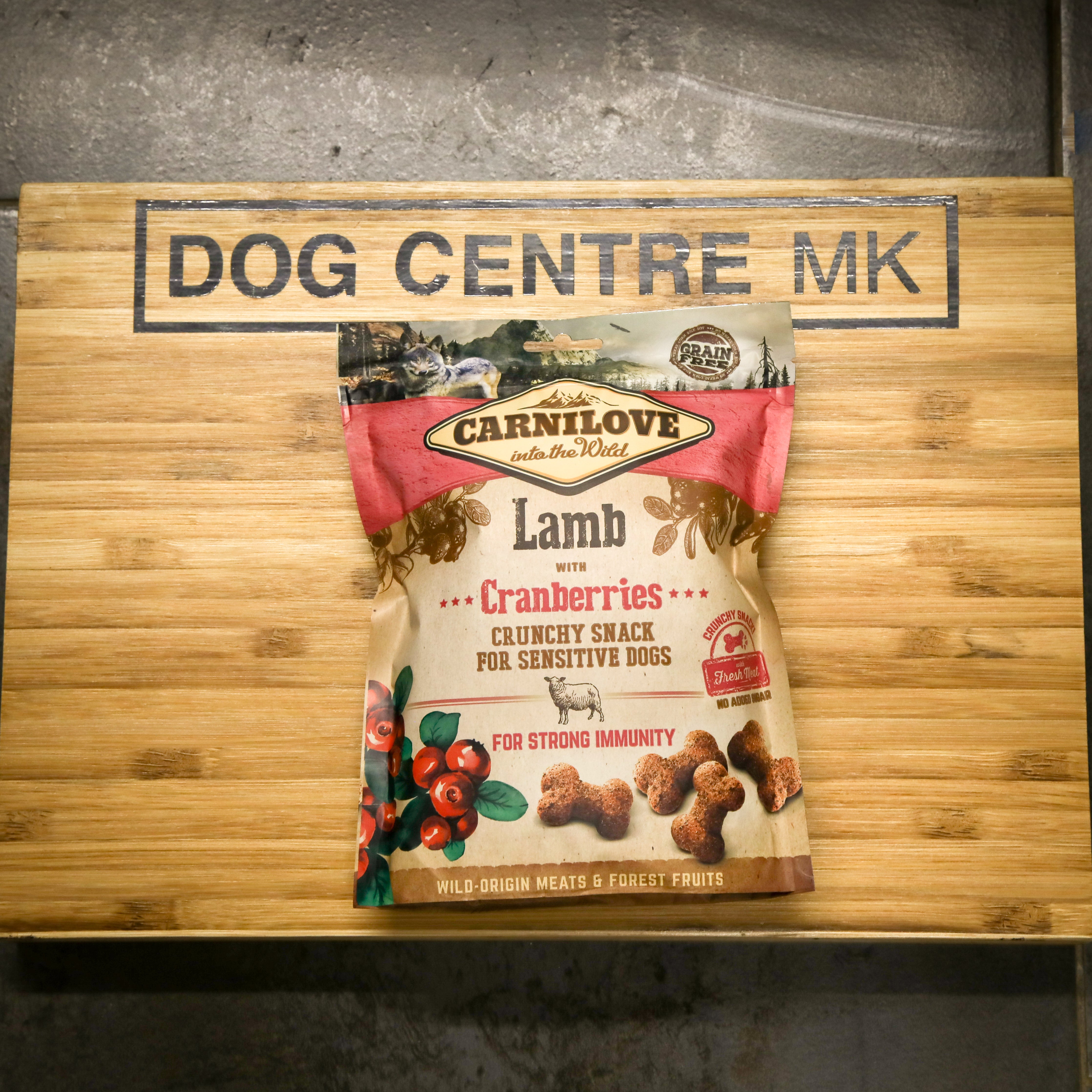Carnilove Lamb with Cranberries dog snack package on a wooden board with 'DOG CENTRE MK' branding.