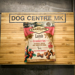 Carnilove Lamb with Cranberries dog snack package on a wooden board with 'DOG CENTRE MK' branding.