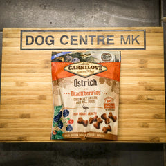Carnilove Ostrich with Blackberries snack package on a wooden board with 'DOG CENTRE MK' branding.