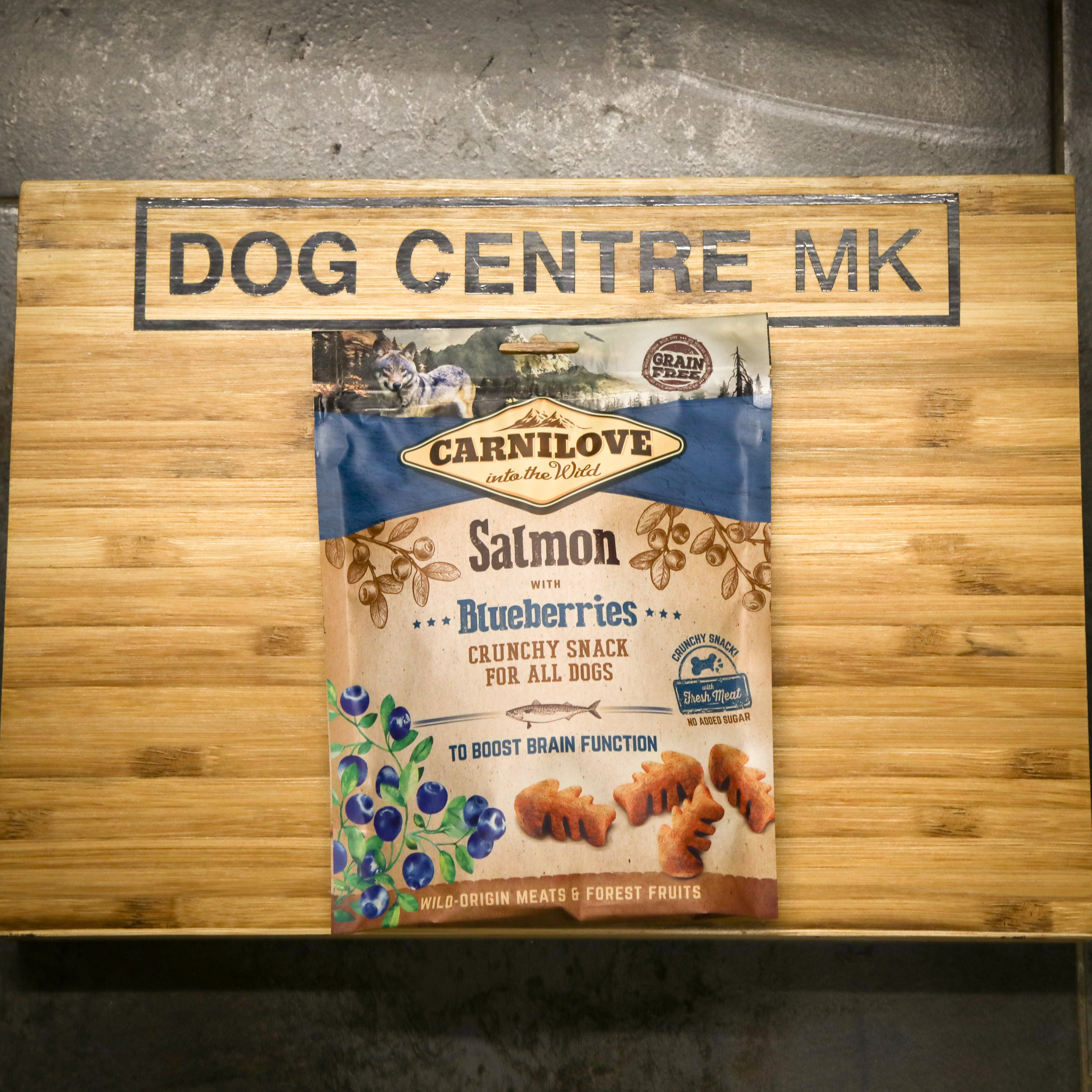 Carnilove salmon with blueberries crunchy snack package on a wooden board with 'DOG CENTRE MK' branding.