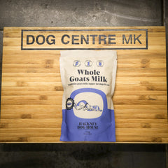 Bag of Hackney Dog House Whole Goats Milk on a wooden surface with 'Dog Centre MK' sign.