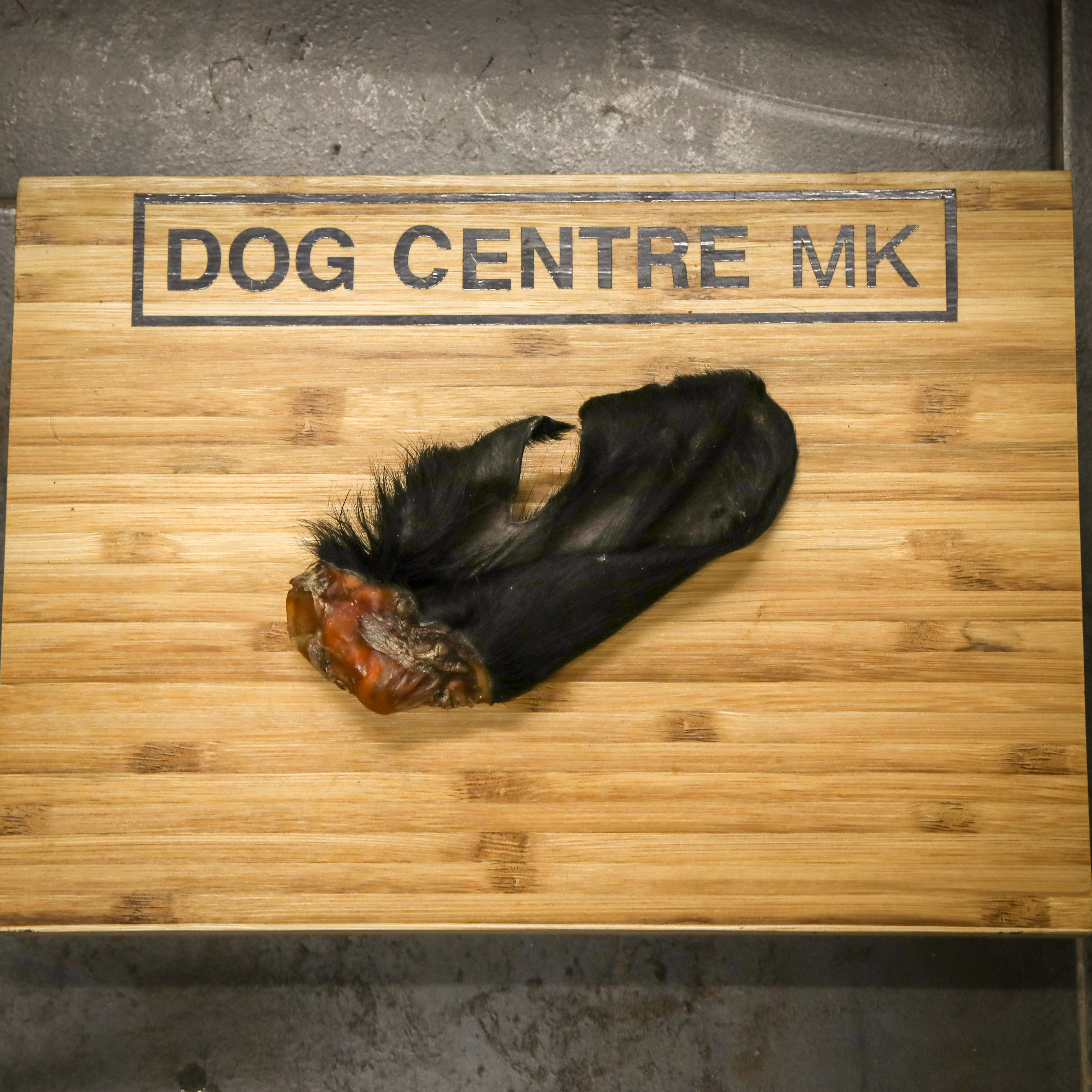 Black hairy cow ear on a wooden board with 'DOG CENTRE MK' branding.