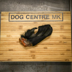 Black hairy cow ear on a wooden board with 'DOG CENTRE MK' branding.