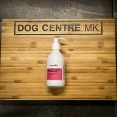 Bottle of muscle and joint supplement for pets on a wooden board with 'DOG CENTRE MK' branding.