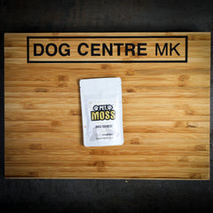 A sealed white bag labeled 'Pet Moss' from Dog Centre MK, placed on a wooden surface.