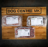 Packaged chicken products labeled 'DOG CENTRE MK' displayed on a wooden surface.